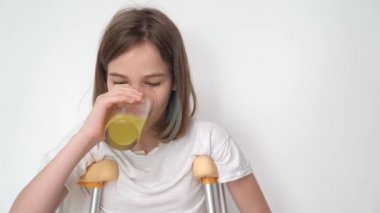 Koltuk değnekli genç bir kız bardaktan meyve suyu içer. İlaç ve vitamin alıyordum. Düşük hareketli insanların rahatsızlığı. Hasta tedavisi ve bakımı. Hane meselelerinde engellilerin özerkliği.