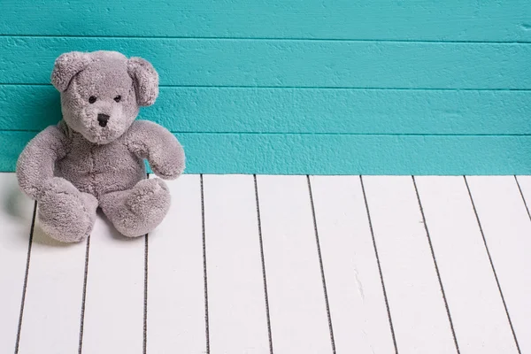 Teddy urso sentado no chão de madeira branco com fundo azul-verde solitário — Fotografia de Stock