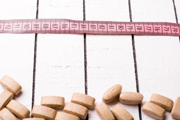 Pastillas y cinta métrica rosa sobre el fondo blanco de madera — Foto de Stock