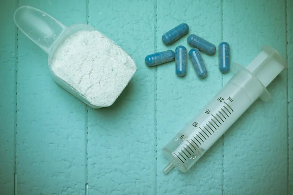 Контейнер з білком молочної сироватки, порожні ін'єкції та таблетки. Крупним планом. Синій фон — стокове фото