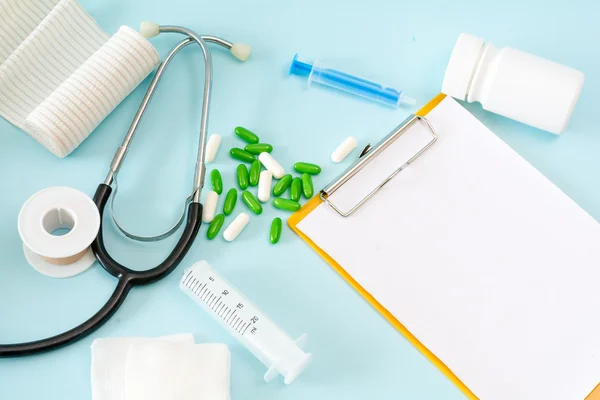 Imagem conceitual médica com um estetoscópio, pílulas, injeção, gaze, gesso adesivo, garrafa, folha de área de transferência vazia . — Fotografia de Stock