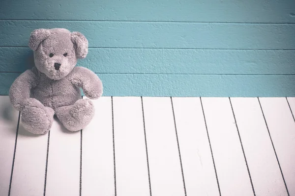Mavi-yeşil arka planlı yalnız beyaz ahşap zemin üzerinde oturan bir oyuncak ayı — Stok fotoğraf