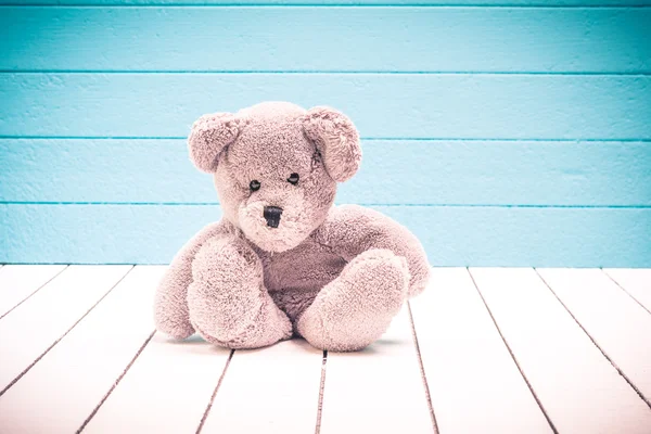 Teddy urso sentado no chão de madeira branco com fundo azul-verde solitário — Fotografia de Stock