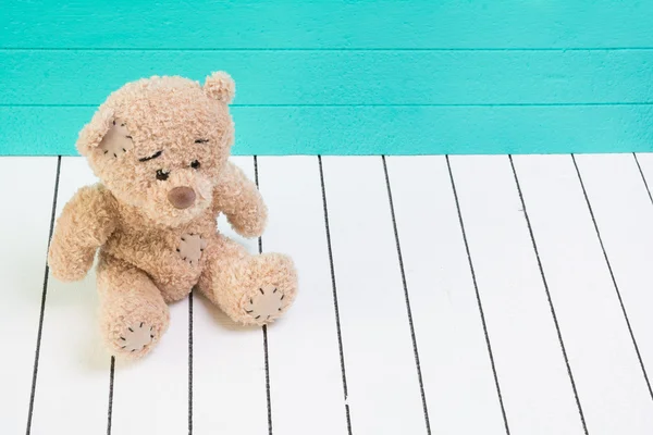 Teddy urso sentado no chão de madeira branco com fundo azul-verde solitário — Fotografia de Stock