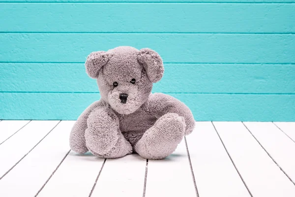 Teddy urso sentado no chão de madeira branco com fundo azul-verde solitário — Fotografia de Stock