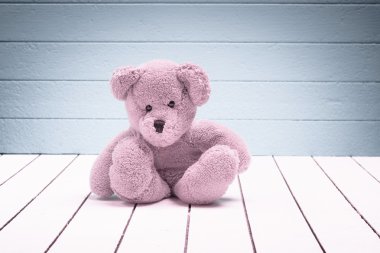 Mavi-yeşil arka planlı yalnız beyaz ahşap zemin üzerinde oturan bir oyuncak ayı