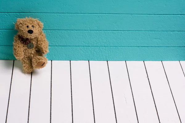 Mavi-yeşil arka planlı yalnız beyaz ahşap zemin üzerinde oturan bir oyuncak ayı — Stok fotoğraf