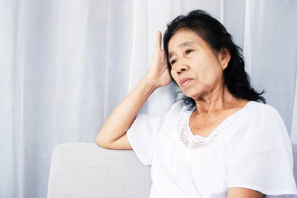 stressed old Asian woman sitting lonely at home feeling sad and depressed