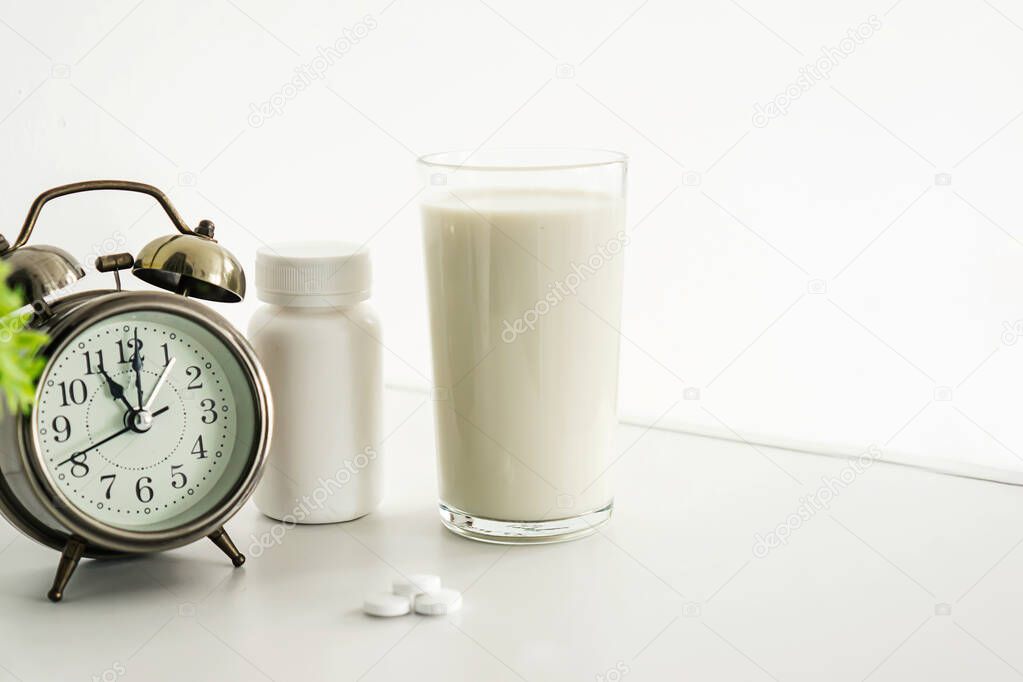glass of milk and bottle of antibiotics pills ,alarm clock on table