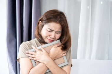 Yas tutan Asyalı bir kadın, sevdiğinin fotoğrafı elindeyken ağlıyor. Derin bir keder, üzüntü ve duygusal acı hissediyor. Kaybı, yalnızlığı ve yas tutmayı sembolize ediyor. 