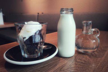 Yumuşak kremalı şık bir kahve bloğu. Soğuk süt ve şeffaf şuruplu buzlu sade kahve. Ahşap masa ve toprak tonlama tasarımlı rahat bir restoran ve kafe..