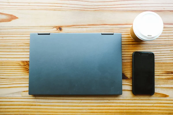 Kapalı dizüstü bilgisayar, kahve ve telefon ahşap bir masada.