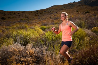 Blonde female trail runner running through a mountain landscape clipart