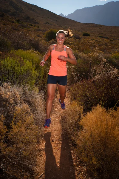 Blonde female trail runner running through a mountain landscape — Stock Photo, Image