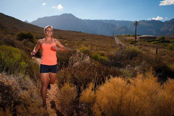Blonde female trail runner running through a mountain landscape — Stock Photo, Image