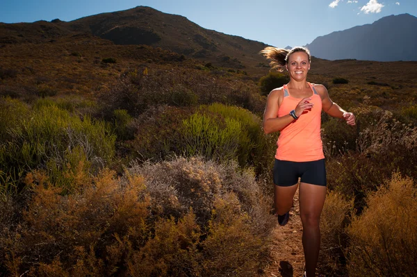 Blonde female trail runner running through a mountain landscape — Stock Photo, Image