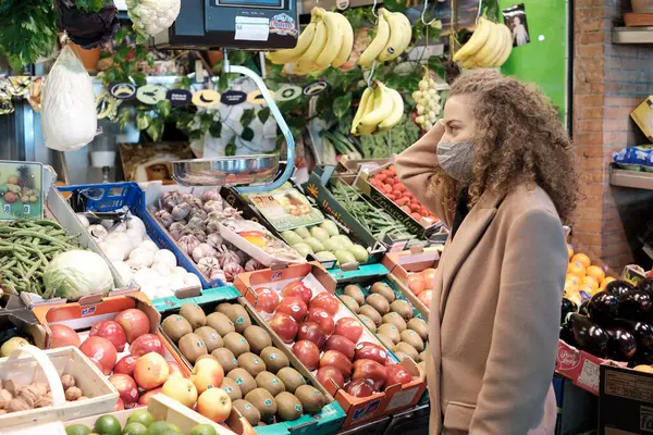 woman wear face mask is buying fresh fruits and vegetables on a farmer market in Seville