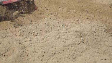 Çiftçi bahçedeki toprağı bir dümen-motor ekicisi kullanarak işliyor. Şapkalı ve lastik çizmeli adam. 4K görüntüsü. Yan görünüm