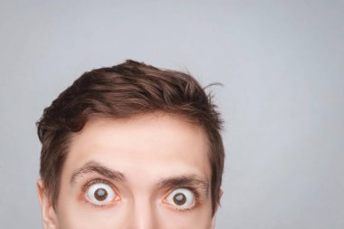 Adamın gözleri arka plandaki ışığa bakıyor. Metin veya nesne için boş yer. Yuvarlak gözlü, yarım kafalı, şok olmuş genç adamın yakın çekimi. Önüne bak.