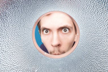 Adam bardağın içine ya da yuvarlak metal tüpe bakıyor. Yuvarlak gözlü ve ağzı açık genç adamın yakın plan çekimi.. 