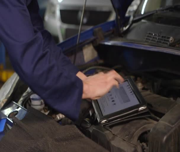 Mechanic using a digital tablet while doing routine maintenance on a car in a ga — Stock Video