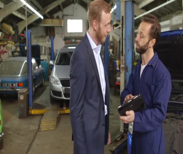 Mechanic explaining expenses for car repair to his customer — 图库视频影像