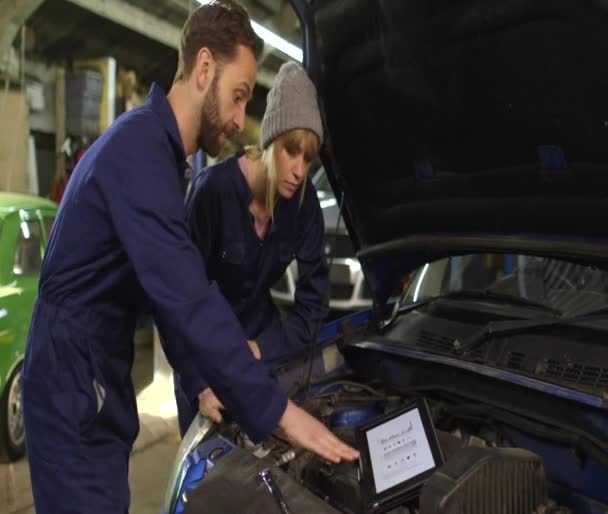 Auto-mechanic en een vrouwelijke stagiair tijdens een workshop voor een auto — Stockvideo