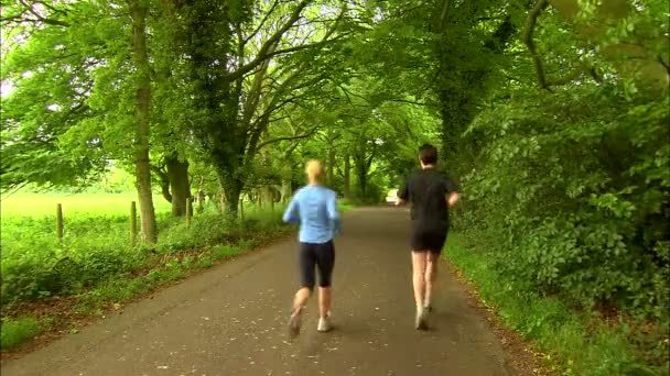 Man och kvinna jogga förbi kameran ner country lane — Stockvideo