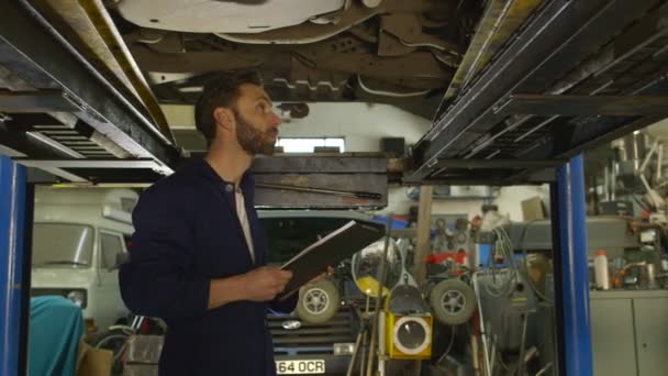 Mechanic inspecteert de auto onderstel manier en maakt een opmerking — Stockvideo