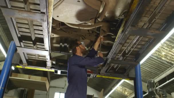 Porträtt av en ung mekaniker arbetar under en bil — Stockvideo