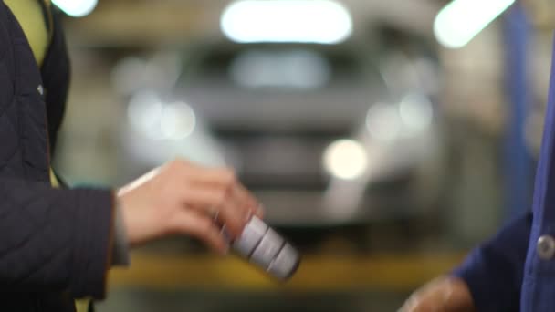 Close Up shot of a woman's hand handing over a car key to a mechanic in garage — Stock Video