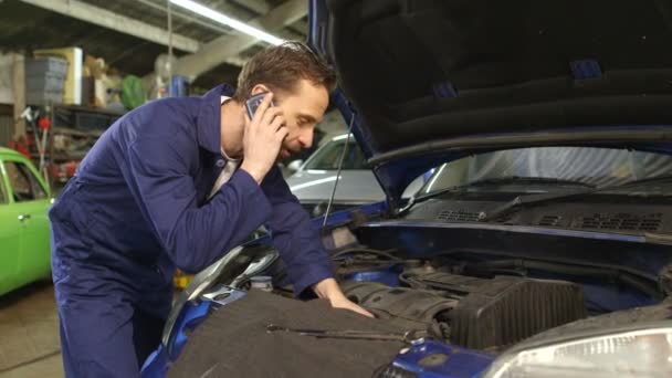 Механик разговаривает по мобильному телефону с владельцем автомобиля во время ремонта автомобиля — стоковое видео
