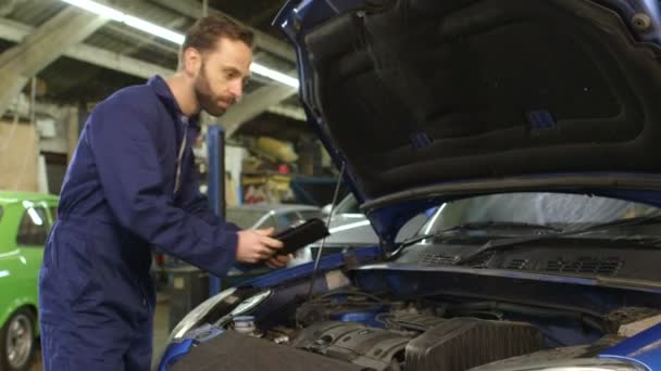 Mecánico usando una tableta digital para un chequeo de mantenimiento rutinario en un automóvil — Vídeos de Stock