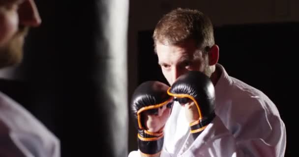 Entraîneur avec un jeune athlète pratique la boxe avec un sac de boxe — Video