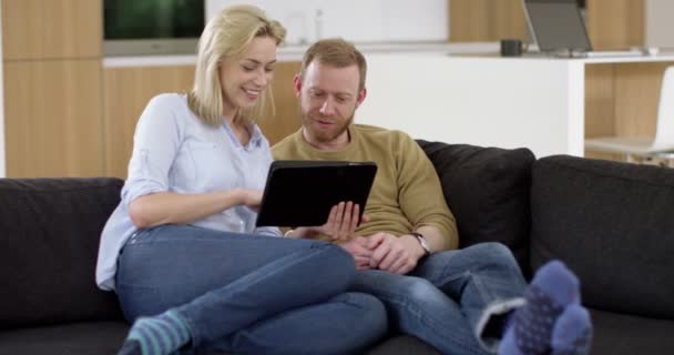 Atractiva pareja joven en la sala de estar, websurf en Internet utilizando tableta en el hogar contemporáneo, en cámara lenta — Vídeos de Stock