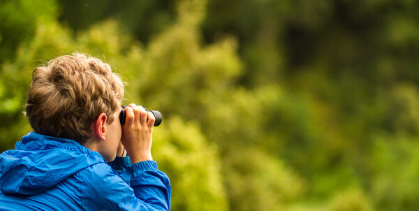 young boy bird watching in a forest