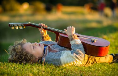 Genç çocuk günbatımında bir gitar çalmak çim döşeme