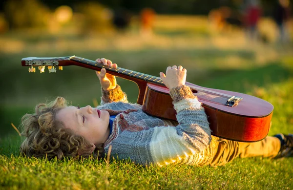 Genç çocuk günbatımında bir gitar çalmak çim döşeme