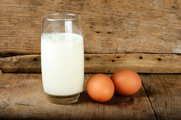 Sklo s mlékem a vejcem na dřevěné pozadí — Stock fotografie