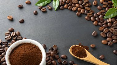 Koyu dokulu bir yüzey ustalıkla kavrulmuş kahve çekirdekleri öğütülmüş kahve bardağı ve içinde kahve tozu bulunan tahta bir kaşık ile düzenlenir.