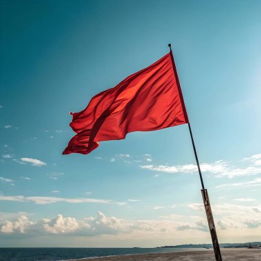 Mavi deniz ve gökyüzü bulutlu bir gökyüzünün altında uzanan plajda çarpıcı bir kırmızı bayrak dalgalanıyor.