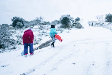 Çocuklar karda kızakla oynuyorlar.