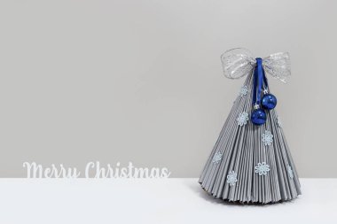 Topları ve kurdelesi olan gri Noel ağacı. Mutlu Noeller yazılı.