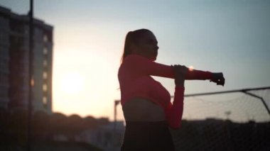 Spor giyim sektöründe spor giyinen kadın stadyumdaki yeşil futbol sahasında, beyaz işaretli spor minderleri üzerinde çeşitli egzersizler yapıyor. Açık hava sporları. Online eğitim. Sıcak yaz günü. sağlıklı yaşam tarzı kavramı