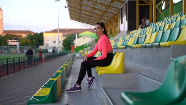 Spor Üniformalı Güzel Bir Kız Stadyumun Podyumunda Oturuyor Sahaya Doğru — Stok video