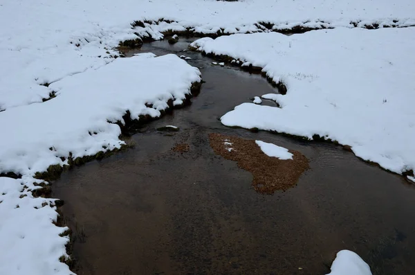 台形の周囲を雪に覆われた山の小川の中の錆びた泥炭水 山の泥炭の春は ストリームや川を供給します これは山の貯水池です — ストック写真