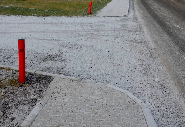 connection of a side dirt road to an asphalt road. the turn is highlighted by a pair of red bollards with reflectors. sidewalks of concrete paving. designation of a side road according to EU standart