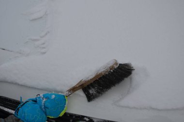 Kış renkli eldivenli küçük çocuk. Eski bir süpürge tutuyor ve bir araba motorunun beyaz kaputundan kar temizliyordu. Babamın araba temizliğiyle ilgileniyorum..
