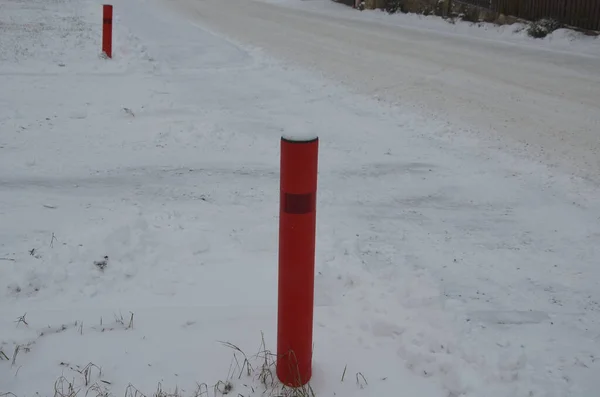 connection of a side dirt road to an asphalt road. the turn is highlighted by a pair of red bollards with reflectors. sidewalks of concrete paving. designation of a side road according to EU standart