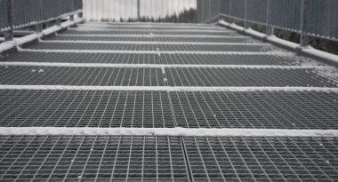 Ağır yük altında bile deformasyona karşı yüksek dirençle kaplı gri karla kaplı merdiven gözlem güvertesi inşaatı. Galvanize çelik kaynaklı zemin ızgarası, korkulukları, manzara haritalı oryantasyon tahtaları.